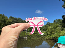 Load image into Gallery viewer, Sticker | D Phi E | Delta Phi Epsilon Pink Bow | Waterproof Vinyl Sticker | White | Clear | Permanent | Removable | Window Cling | Glitter | Holographic